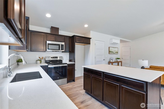 kitchen with light wood finished floors, a wall unit AC, a sink, stainless steel appliances, and recessed lighting