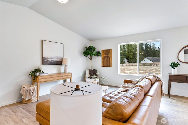 living area featuring baseboards, light wood finished floors, and lofted ceiling