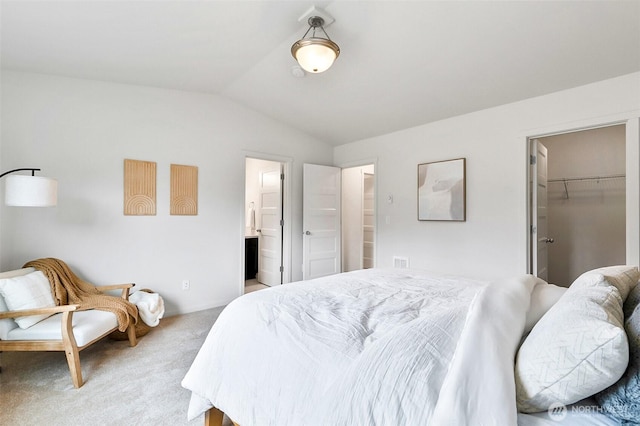 bedroom featuring vaulted ceiling, light carpet, connected bathroom, and a spacious closet