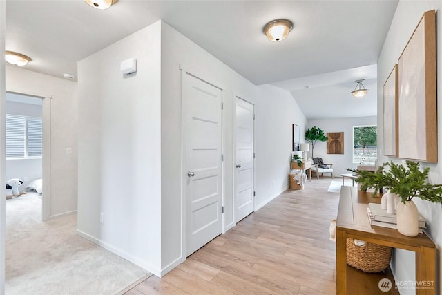 hall with baseboards, vaulted ceiling, and light wood-type flooring