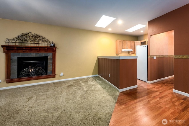 kitchen with a skylight, a tiled fireplace, hardwood / wood-style floors, white fridge, and kitchen peninsula