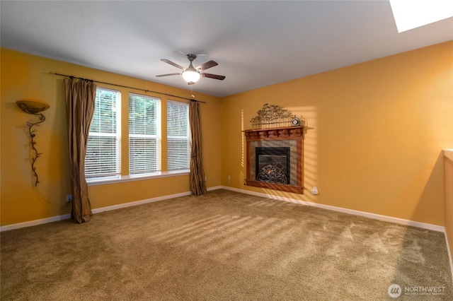 unfurnished living room featuring a tile fireplace, a skylight, ceiling fan, and carpet floors