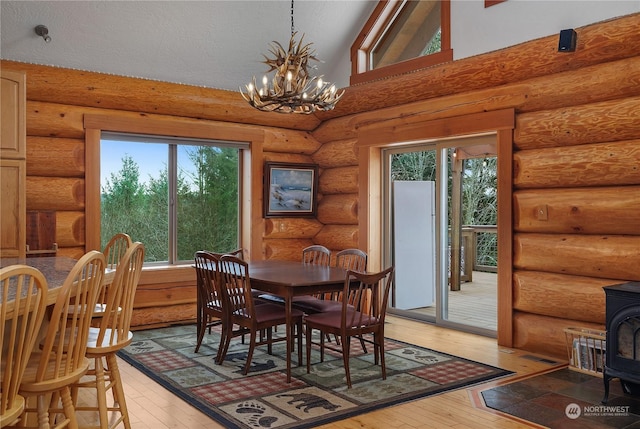 dining area with a chandelier, high vaulted ceiling, light hardwood / wood-style flooring, and a wood stove