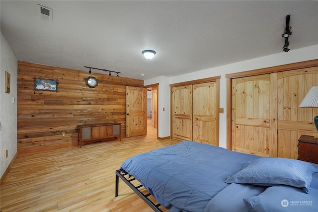 bedroom with two closets, wood walls, wood-type flooring, and track lighting