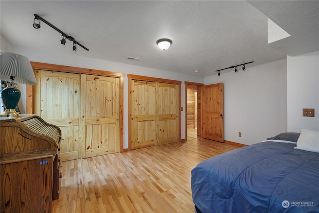 bedroom featuring a textured ceiling, track lighting, light hardwood / wood-style floors, and two closets