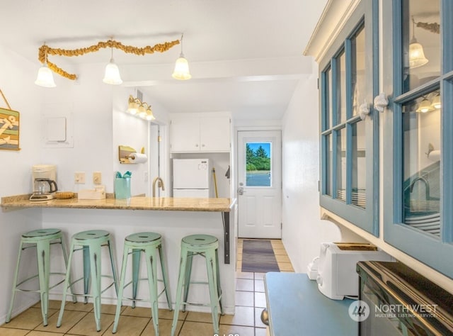 kitchen with hanging light fixtures, a kitchen breakfast bar, light stone counters, white refrigerator, and white cabinets