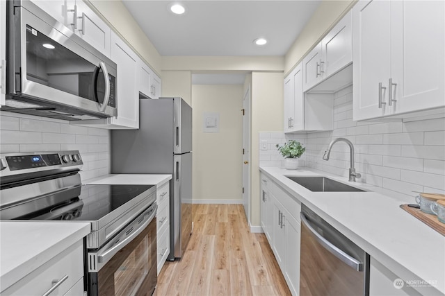 kitchen with decorative backsplash, light wood-type flooring, white cabinets, appliances with stainless steel finishes, and sink