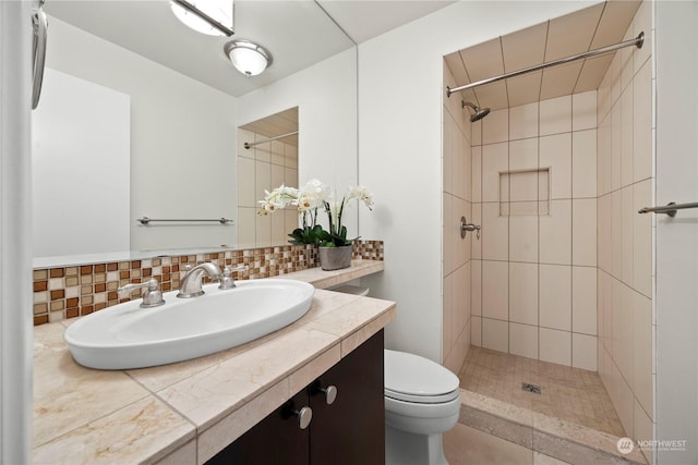 bathroom featuring toilet, a tile shower, tasteful backsplash, and vanity