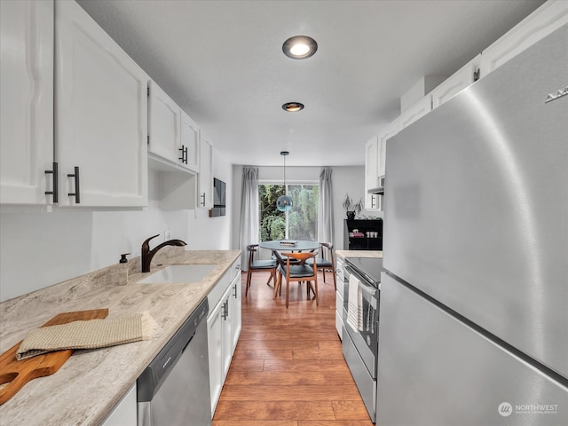 kitchen with white cabinetry, sink, stainless steel appliances, pendant lighting, and light wood-type flooring