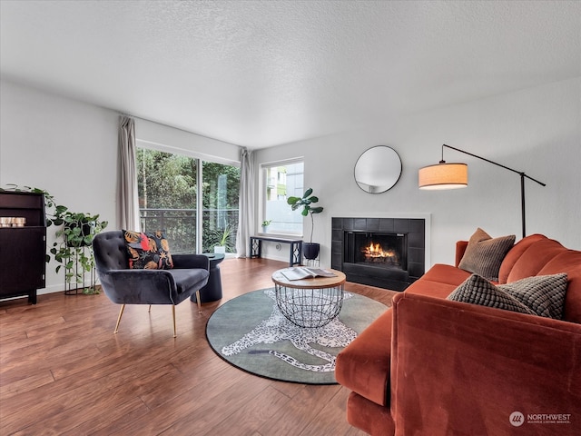 living room featuring a tile fireplace, wood-type flooring, and a textured ceiling