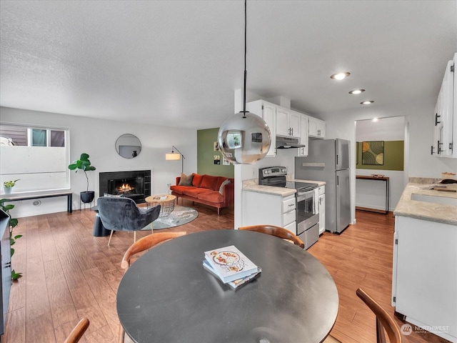 dining room featuring a textured ceiling, light wood-type flooring, and a tiled fireplace