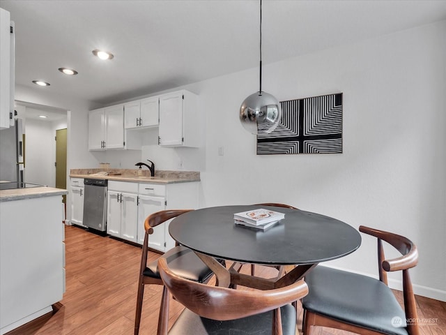 kitchen with appliances with stainless steel finishes, decorative light fixtures, white cabinetry, and light hardwood / wood-style floors