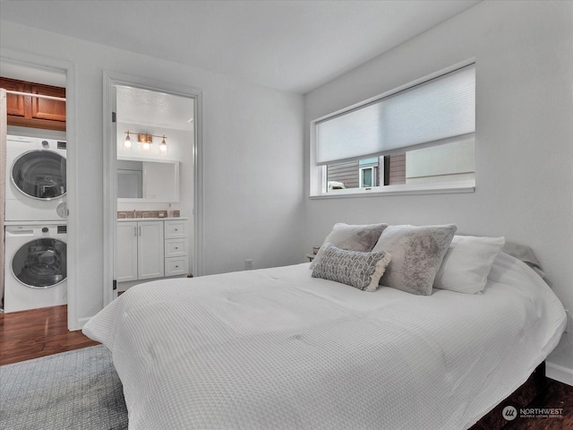 bedroom featuring stacked washing maching and dryer, dark wood-type flooring, and ensuite bathroom