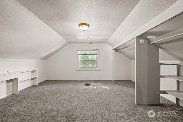 additional living space featuring a textured ceiling, dark carpet, and lofted ceiling