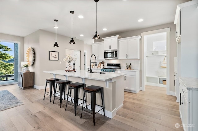 kitchen with stainless steel appliances, white cabinetry, hanging light fixtures, and a kitchen island with sink