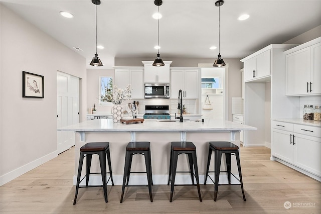 kitchen with stainless steel appliances, a center island with sink, and pendant lighting