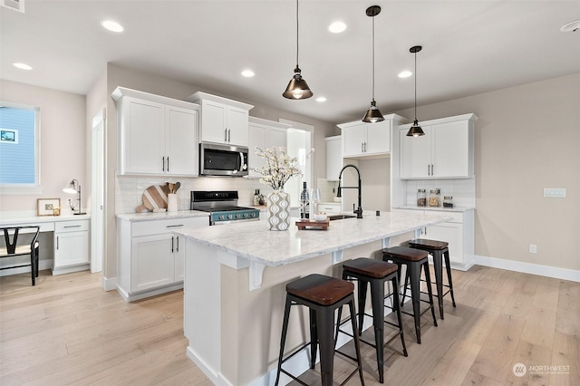 kitchen with appliances with stainless steel finishes, hanging light fixtures, a center island with sink, and white cabinets