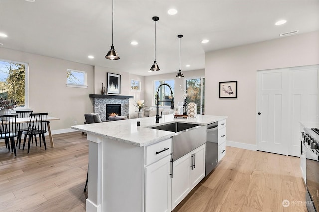 kitchen featuring white cabinetry, light stone counters, hanging light fixtures, stainless steel dishwasher, and an island with sink