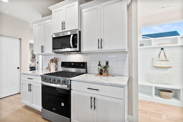 kitchen with light hardwood / wood-style flooring, white cabinets, stainless steel appliances, light stone countertops, and backsplash