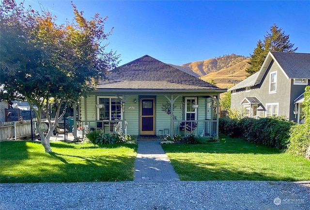 bungalow-style home with covered porch, a mountain view, and a front lawn