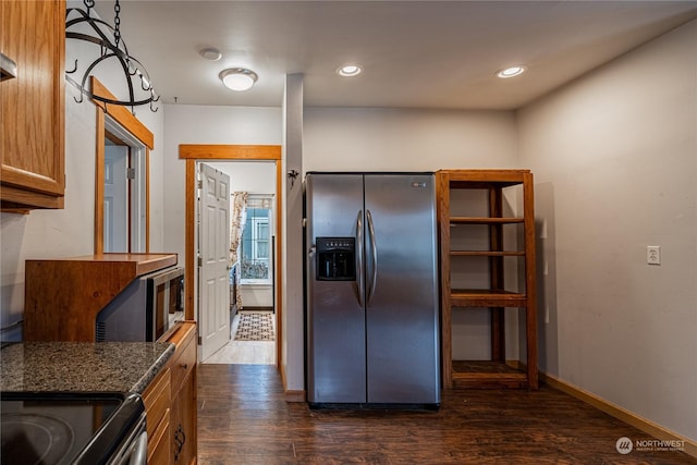 kitchen featuring stainless steel appliances, decorative light fixtures, dark stone countertops, and dark wood-type flooring