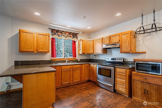 kitchen with appliances with stainless steel finishes, kitchen peninsula, dark wood-type flooring, a kitchen bar, and sink