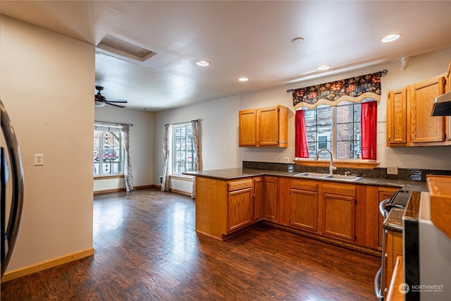 kitchen with kitchen peninsula, stainless steel stove, dark hardwood / wood-style floors, ceiling fan, and sink