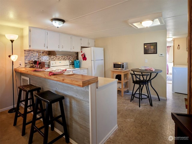 kitchen with a kitchen bar, tasteful backsplash, white appliances, white cabinets, and washer / dryer