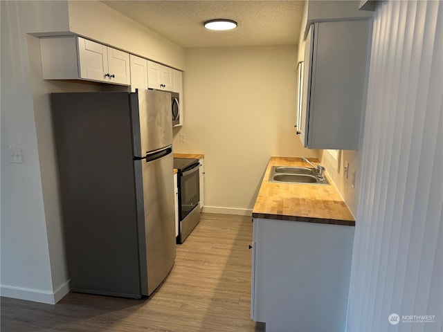 kitchen featuring stainless steel refrigerator, electric range, sink, butcher block counters, and white cabinets