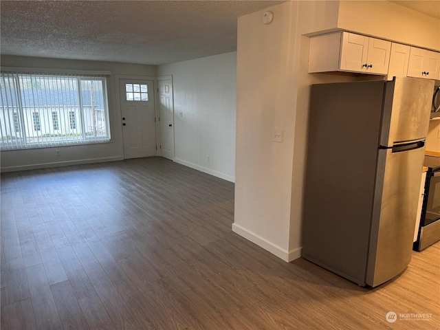 interior space featuring a textured ceiling, white cabinetry, stainless steel refrigerator, and light hardwood / wood-style floors