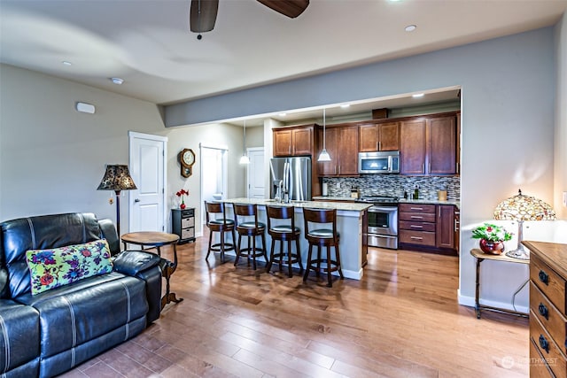 kitchen featuring backsplash, a center island with sink, hanging light fixtures, a breakfast bar area, and stainless steel appliances