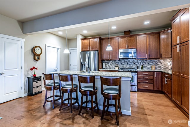 kitchen with light stone countertops, a kitchen island with sink, hanging light fixtures, and stainless steel appliances