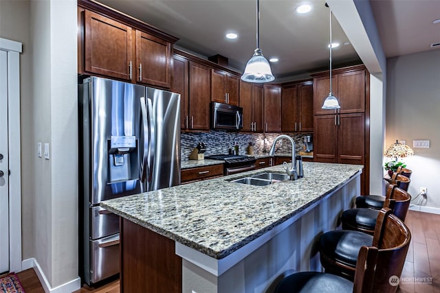 kitchen with hanging light fixtures, light stone counters, sink, and stainless steel appliances