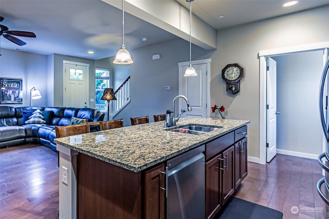 kitchen with a center island with sink, sink, stainless steel dishwasher, dark stone countertops, and decorative light fixtures