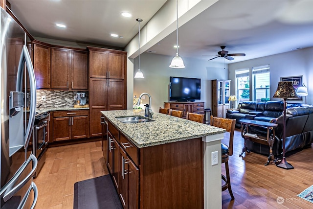 kitchen featuring sink, an island with sink, appliances with stainless steel finishes, tasteful backsplash, and light stone counters