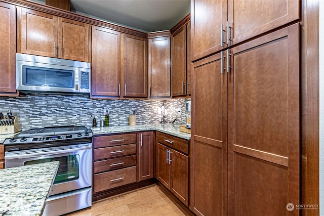 kitchen featuring decorative backsplash, light stone countertops, light hardwood / wood-style flooring, and appliances with stainless steel finishes