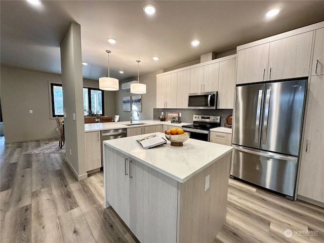 kitchen with appliances with stainless steel finishes, decorative light fixtures, sink, light hardwood / wood-style floors, and kitchen peninsula