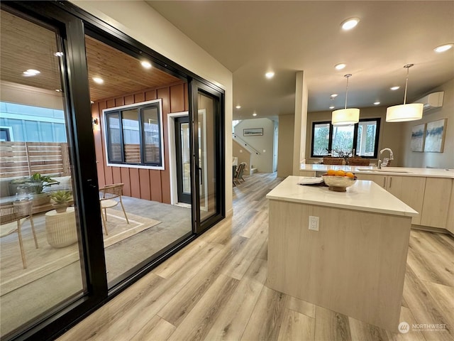 kitchen featuring sink, a center island, light brown cabinetry, decorative light fixtures, and light wood-type flooring