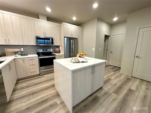 kitchen with appliances with stainless steel finishes, a center island, light wood-type flooring, and decorative backsplash