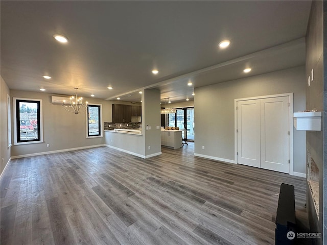 unfurnished living room with an AC wall unit, a chandelier, plenty of natural light, and wood-type flooring