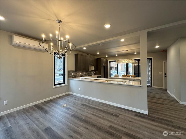 kitchen featuring an AC wall unit, kitchen peninsula, decorative backsplash, a wealth of natural light, and dark brown cabinetry