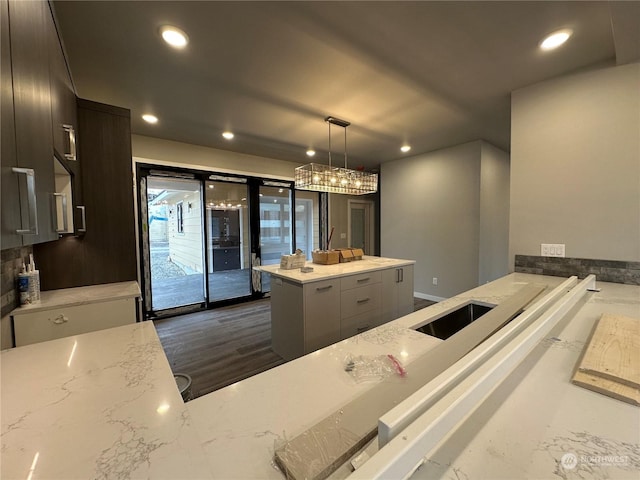 kitchen featuring sink, a kitchen island, hanging light fixtures, and light stone countertops