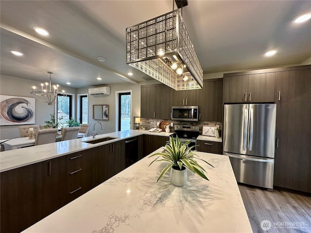 kitchen with appliances with stainless steel finishes, sink, a wall mounted AC, decorative backsplash, and a notable chandelier