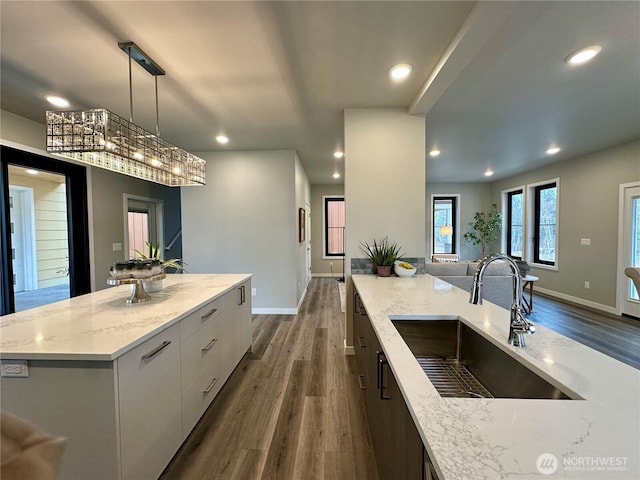 kitchen featuring sink, white cabinetry, a center island, hanging light fixtures, and light stone countertops