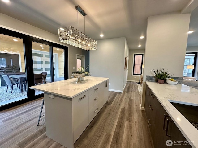 kitchen with white cabinetry, hanging light fixtures, hardwood / wood-style flooring, a center island, and light stone countertops