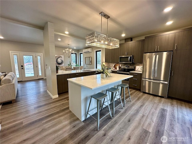 kitchen with stainless steel appliances, dark brown cabinetry, a wall mounted air conditioner, decorative light fixtures, and kitchen peninsula