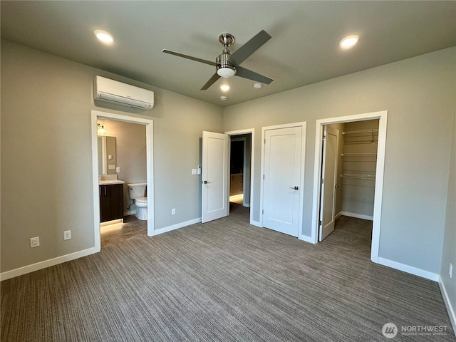 unfurnished bedroom featuring ceiling fan, ensuite bath, a wall mounted AC, and dark carpet