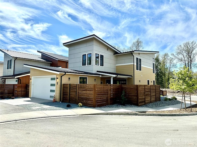 view of front of property with an attached garage, driveway, fence private yard, and metal roof