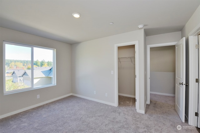 unfurnished bedroom with light carpet, a walk in closet, and a closet