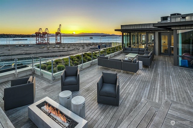 deck at dusk featuring a water view and an outdoor living space with a fire pit